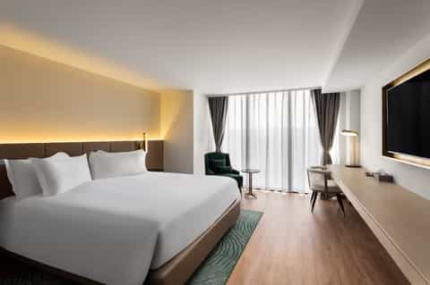 Modern hotel bedroom with king bed, floor-to-ceiling windows, and contemporary furnishings