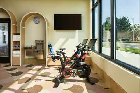 Spin bike fitness studio with arched wooden alcove, storage, TV screen, and large windows with street views