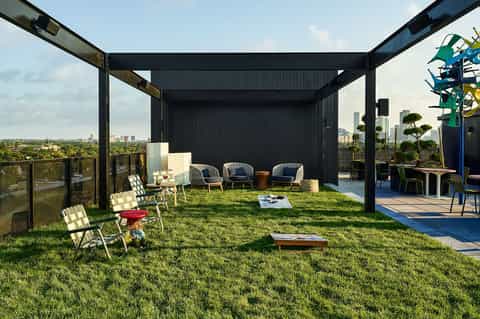 Rooftop terrace with black pergola, grass lawn, blue chairs, and city skyline view