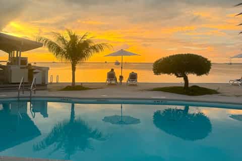 Beachfront pool at sunset with golden sky, palm trees, lounge chairs, and ocean view