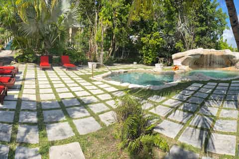 Tropical garden pool area with natural rock features, red loungers, and lush palm trees