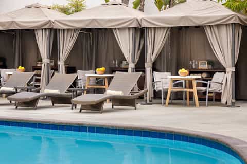 Resort pool deck with cabanas, lounge chairs, and shaded seating areas by the water