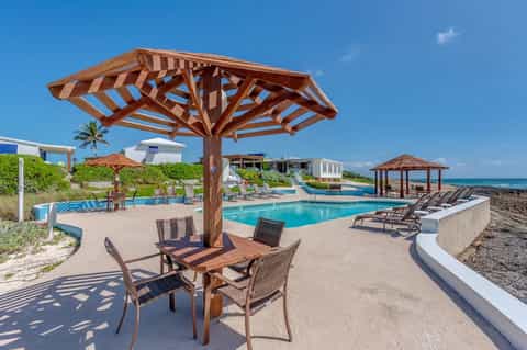 Beachfront pool area with wooden pergola, lounge chairs, and ocean view