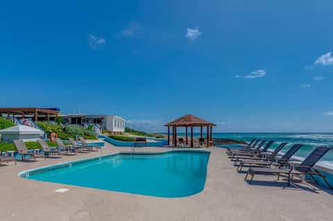 Resort poolside with lounge chairs, gazebo, and ocean view under clear blue sky