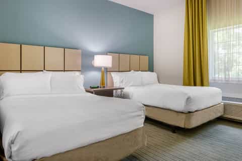 Hotel guest room with two queen beds, teal accent wall, and olive curtains