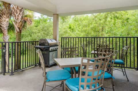Covered patio with outdoor dining table, gas grill, and chairs overlooking lush green landscape