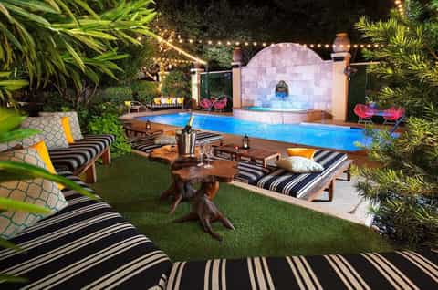 Nighttime resort pool area with striped loungers, tropical plants, illuminated water features, and fire pit