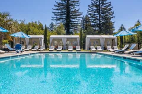 Resort outdoor swimming pool with turquoise water, white cabanas, loungers, and tall pine trees