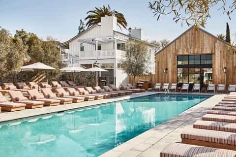 Resort pool area with loungers, umbrellas, modern wooden pavilion, and white building