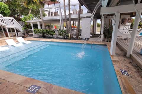Rectangular swimming pool with lounge chairs and covered structures in a tropical resort setting