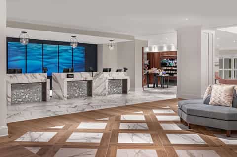 Upscale hotel lobby featuring marble check-in desk, herringbone wood flooring, blue water view windows, and modern furnishings