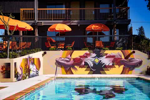 Outdoor pool with colorful mural wall, umbrellas, and upper deck lounge area