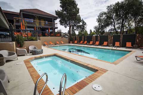 Resort pool and hot tub surrounded by lounge chairs, trees, and multi-story accommodation building
