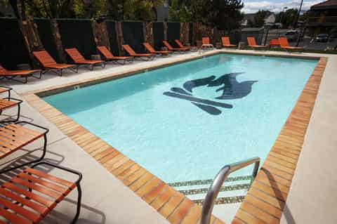 Resort swimming pool with orange lounge chairs, tall hedges, and mountains in background