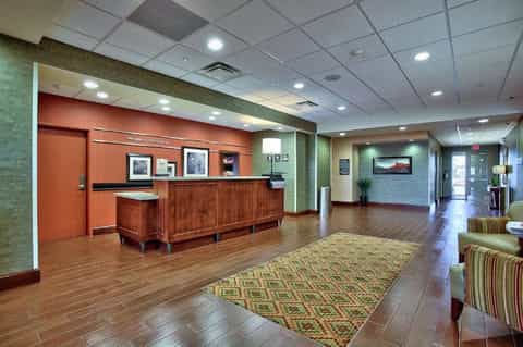 Hotel lobby with orange accent wall, wooden reception desk, and patterned area rug on wood flooring