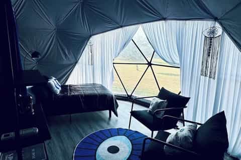 Glamping tent interior with black bed, geometric window frame, and white curtains overlooking fields