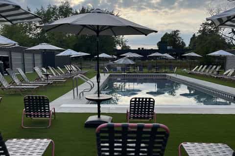 Resort swimming pool surrounded by green lawn, lounge chairs with umbrellas, and changing cabins