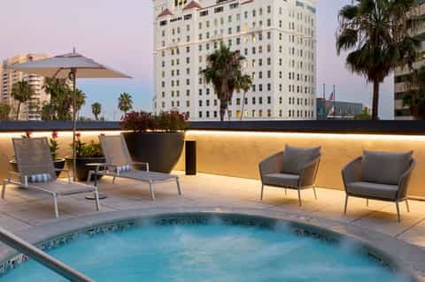 Rooftop pool deck at dusk with lounge chairs, umbrellas, and city skyline views