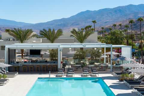 Resort pool with modern bar, white lounge chairs, mountain views, and palm trees