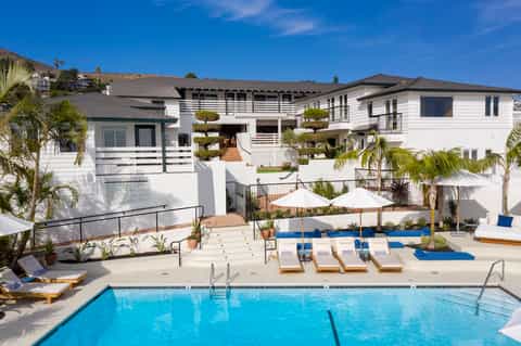 Resort pool area with lounge chairs, umbrellas, and white modern buildings