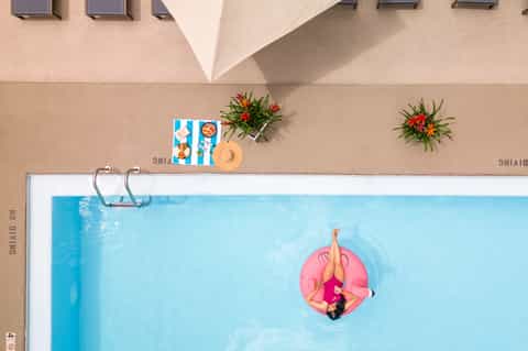 Aerial view of guest floating on pink pool float in bright blue swimming pool