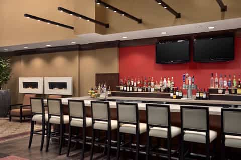 Hotel bar with red accent wall, built-in fireplace, stocked liquor shelves, and bar seating