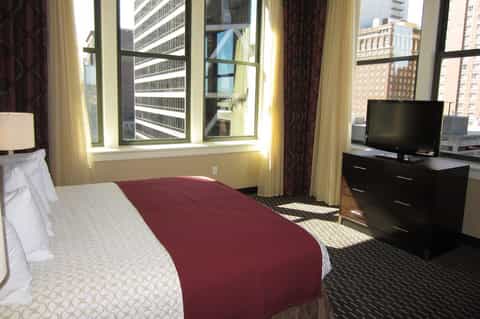 Hotel bedroom with city skyline views, burgundy bedding, and contemporary furnishings