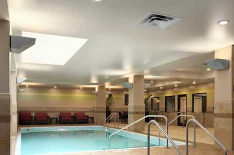 Indoor heated pool with glass walls, ceiling skylights, lounge seating area, and neutral tile flooring