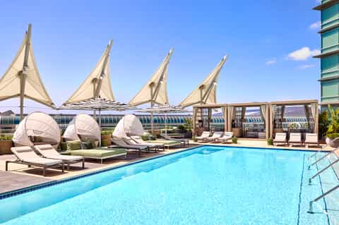 Rooftop pool with sailcloth shade structures, loungers, and modern high-rise building backdrop
