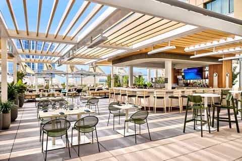 Modern rooftop bar and lounge with wooden pergola, plants, and city skyline views