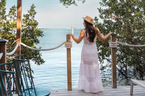 Woman in white dress standing on wooden deck overlooking tropical bay with mangroves