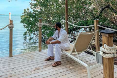 Man relaxing in lounge chair on wooden deck overlooking turquoise water with mangrove trees