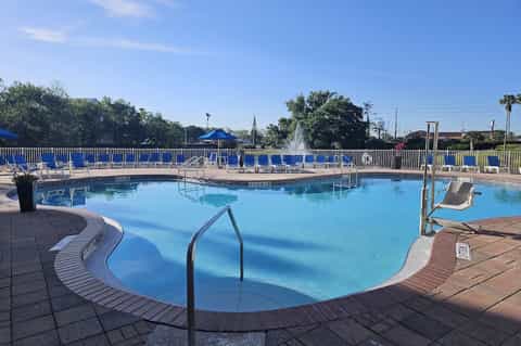 Resort swimming pool with blue lounge chairs, white fence railing, and fountain feature