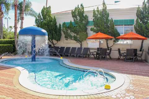 Outdoor pool with water fountain feature, spa hot tub, orange umbrellas, and lounge chairs on brick patio