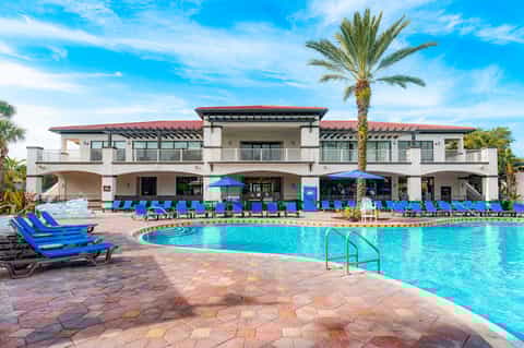 Resort pool complex with bright blue water, loungers, palm trees, and beachfront building