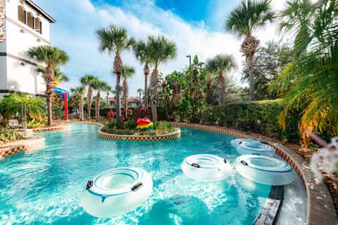 Resort pool with white float rings, palm trees, colorful decorative elements, and lounging areas