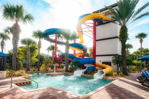 Colorful water slides towering over a tropical pool area surrounded by palm trees