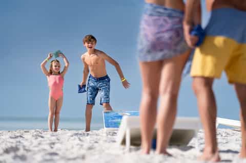 Children playing beach games on sandy shore with ocean and clear sky in background