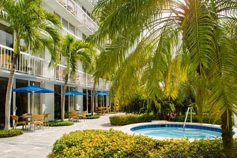 Tropical courtyard with palm trees, blue umbrellas, small pool, and white building facades
