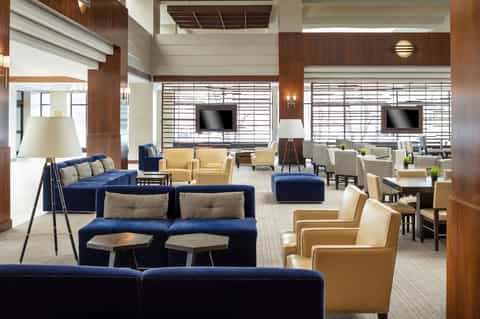 Spacious contemporary hotel lounge with blue and tan seating, wood beams, and large windows