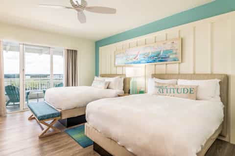Spacious hotel room with two queen beds, balcony view, and coastal blue accent wall