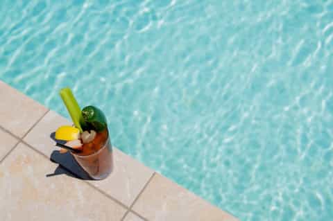 Tropical cocktail with lime garnish on pool deck edge overlooking turquoise water