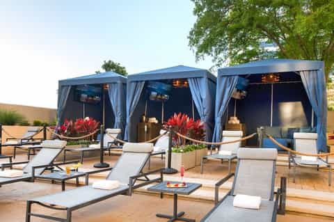 Luxury poolside cabanas with blue curtains, lounge chairs, and red flowering plants on terracotta patio
