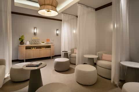 Spa lounge with cream seating, wooden fixtures, ambient lighting, and flowing curtains