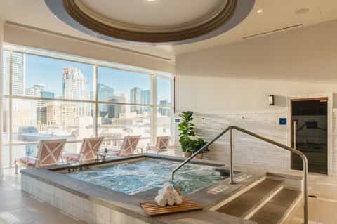 Indoor spa pool with city skyline views, white subway tiles, and lounge chairs