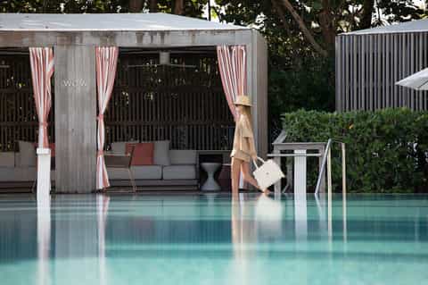 Modern poolside cabana with striped curtains, sofa seating, and green landscaping