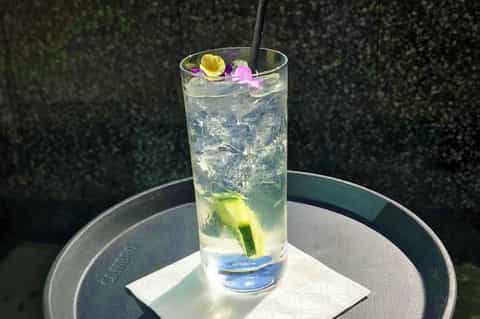 Elegant cocktail with lime slice and edible flowers on a round table with hedged background