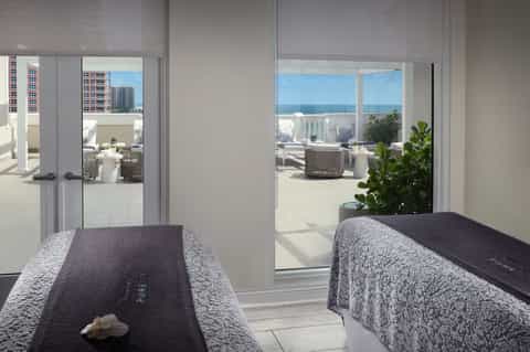Spa treatment room with massage tables and ocean view through glass doors
