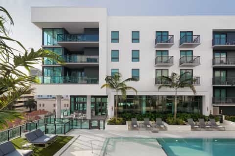 Contemporary residential building with curved balconies, pool area, loungers, and palm trees in daylight