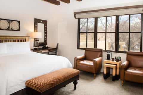 Hotel bedroom with queen bed, leather armchairs, desk, and large windows overlooking landscape